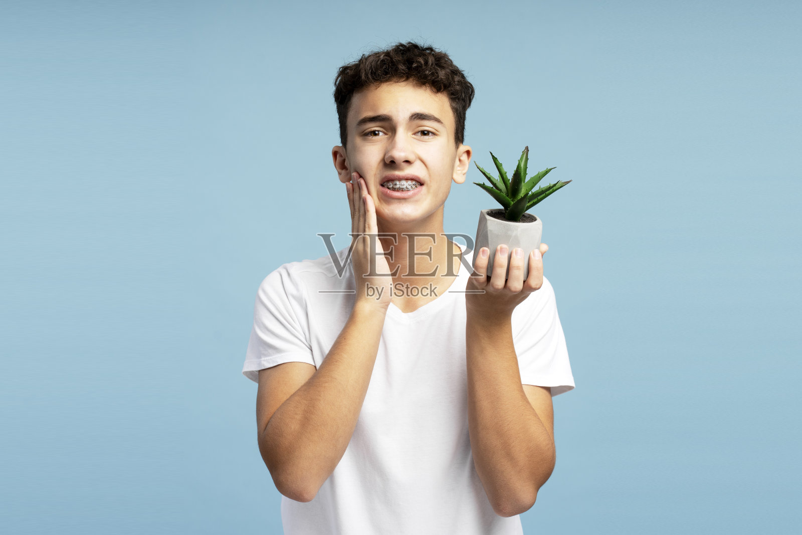 心烦意乱,郁郁不乐的少年带着牙套捧着花盆,摸着脸颊,牙疼照片摄影图片