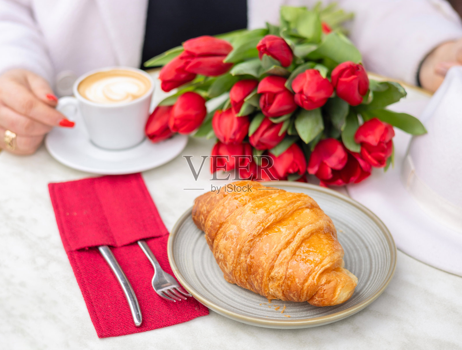 牛角包,红郁金香和卡布奇诺桌在咖啡馆的糕点照片摄影图片