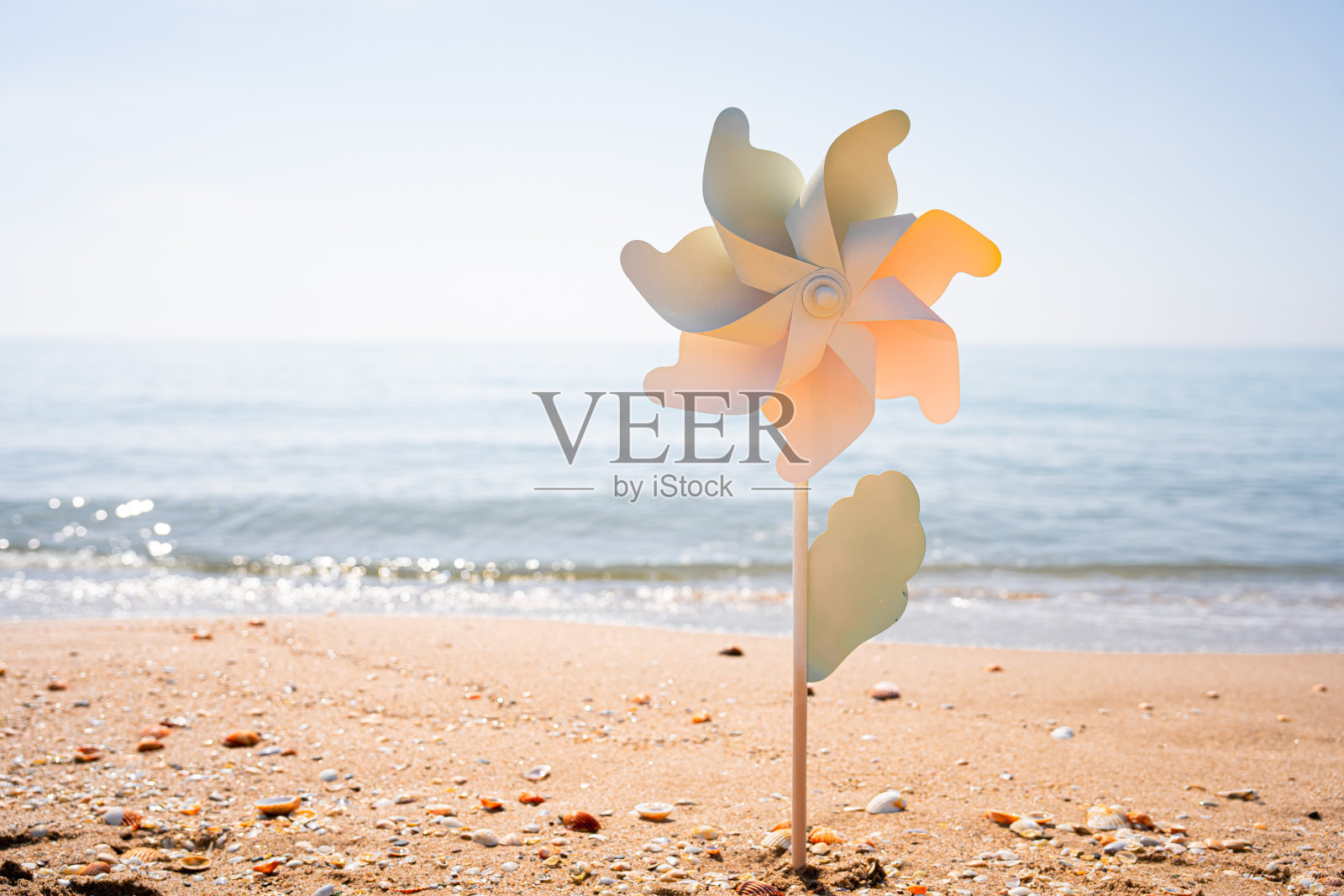 在一个美丽的夏日早晨,以大海为背景的沙滩上,玩具风车卡在沙滩上照片摄影图片