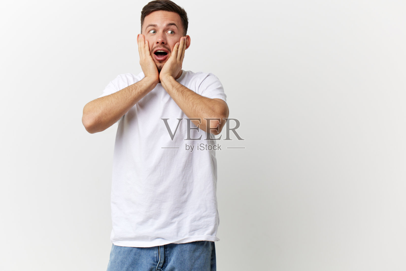 震惊、兴奋、快乐、黝黑、英俊的男人穿着基本的t恤,触摸脸颊,张开嘴,在白色的摄影棚背景上单独摆姿势。复制空间横幅模型。人的情感生活理念照片摄影图片