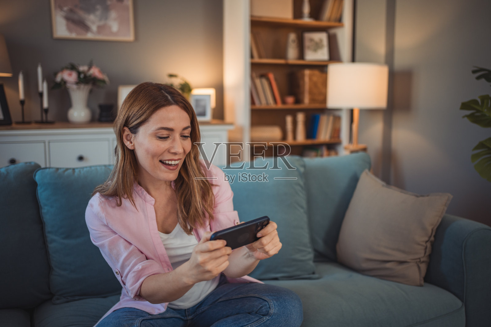 一名成年白人女性坐在家里玩电子游戏,用手机玩网络电子游戏照片摄影图片