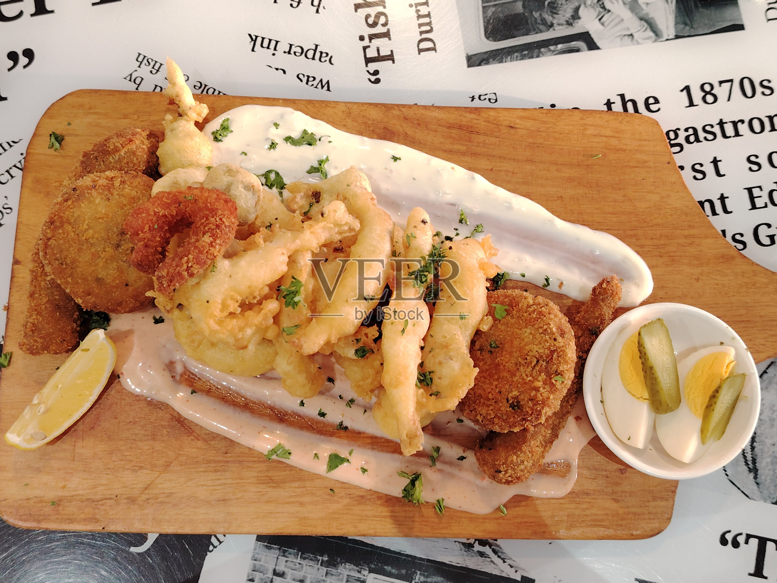 海鲜拼盘,以油炸鱿鱼圈,虾和洋葱圈装饰柠檬在砧板上木制背景。照片摄影图片