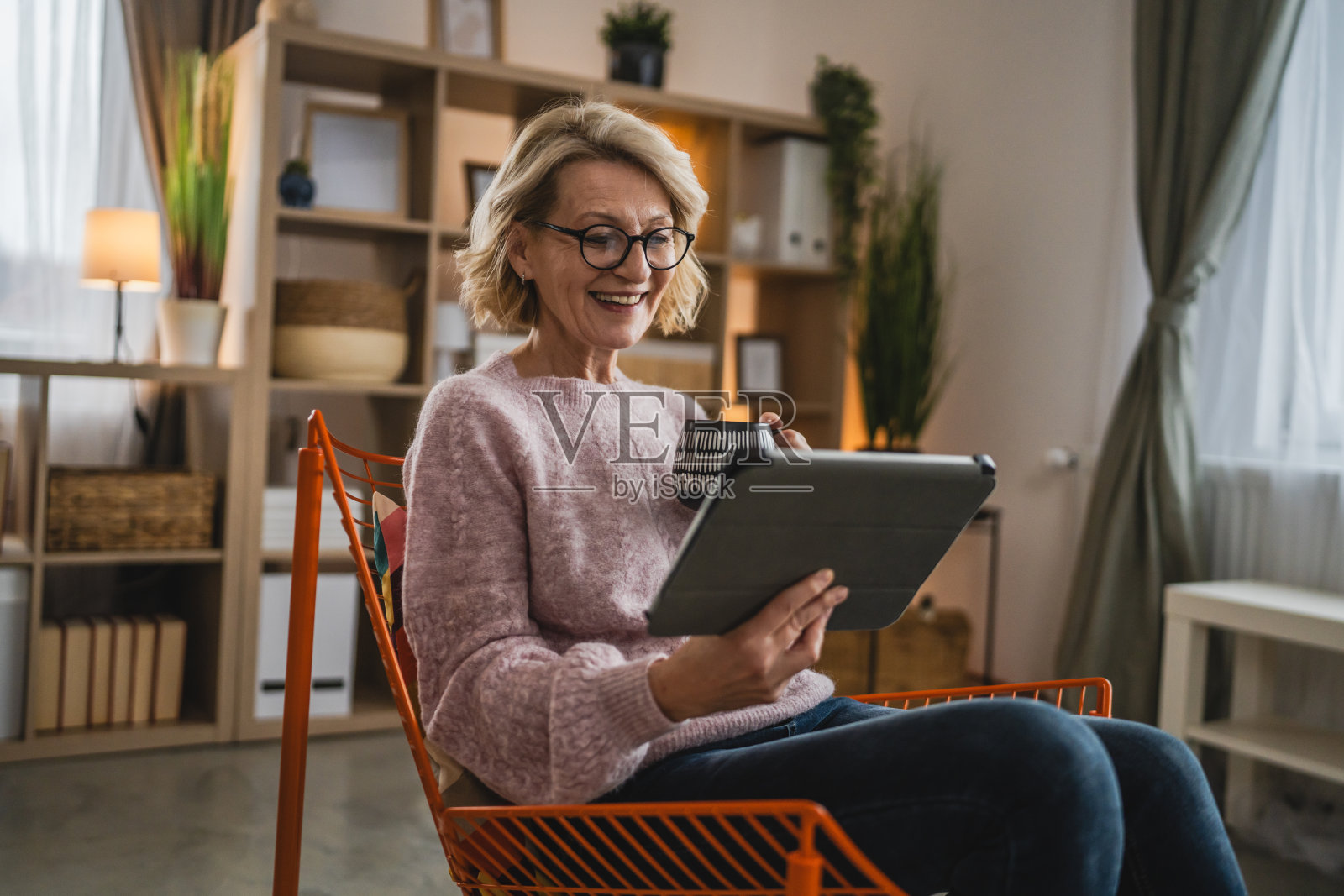 戴眼镜的成熟金发女人在家里使用数码平板电脑照片摄影图片
