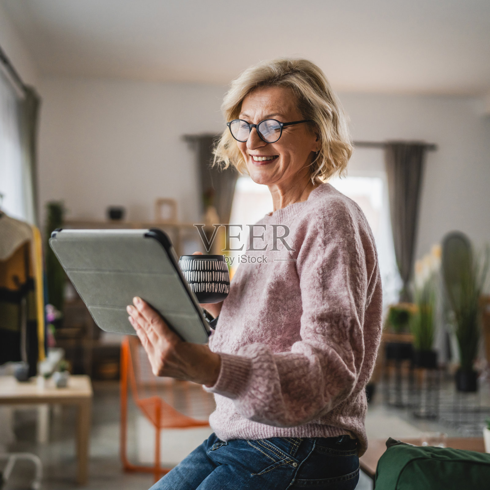 戴眼镜的成熟金发女人在家里使用数码平板电脑照片摄影图片