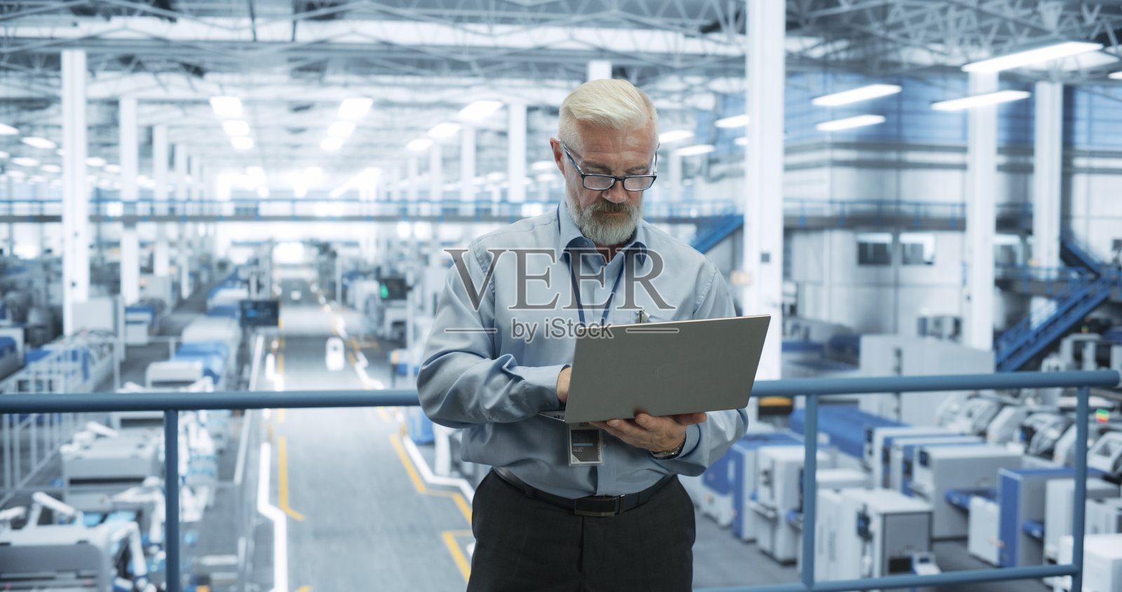 电子厂的高级工程师站在平台上使用笔记本电脑。机器正在进行维护,专家通过在线软件监控更新照片摄影图片