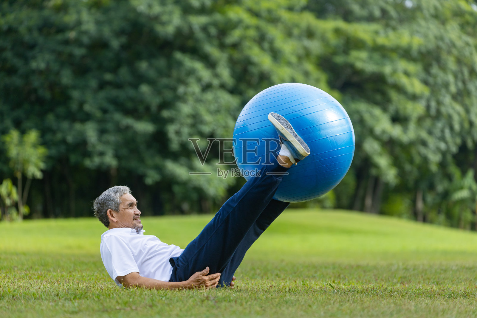 一位亚洲老人正在公园里用瑜伽球锻炼核心身体和腹部肌肉,以增强老年人的健康照片摄影图片