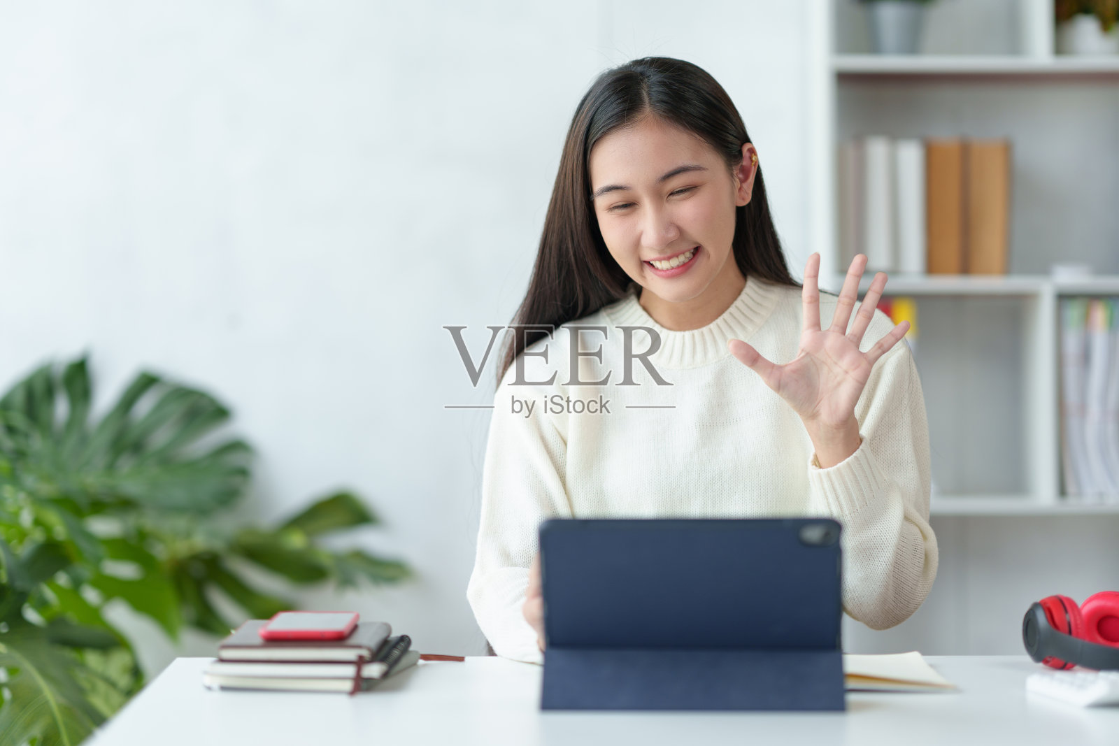 年轻漂亮的亚洲女大学生正在用笔记本电脑和她的同学视频聊天,微笑的面孔和愉快的学习手势。照片摄影图片