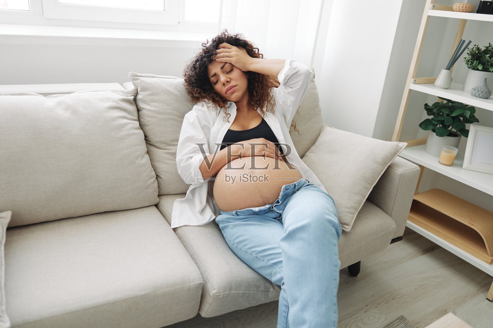 孕妇头痛躺在家里的衬衫和牛仔裤沙发上疲劳和沉重在怀孕前的最后一个月,生活方式困难的母亲,恶心照片摄影图片