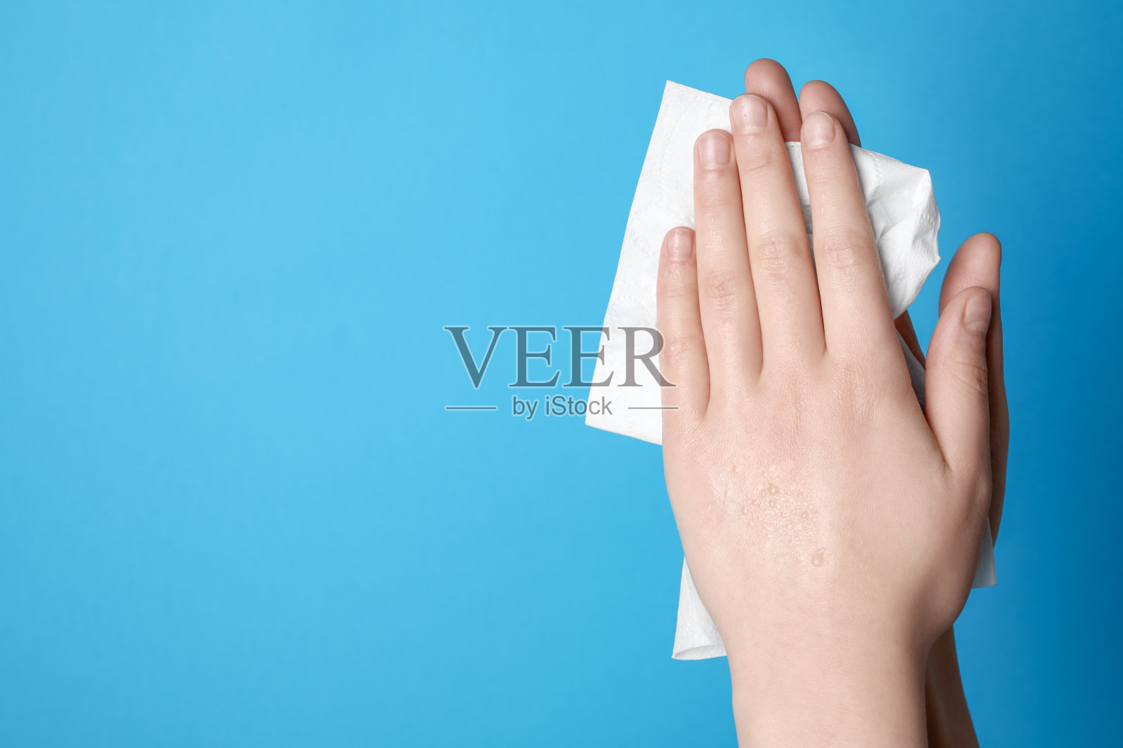 女人用纸巾擦手,浅蓝色背景,特写。文本空间照片摄影图片