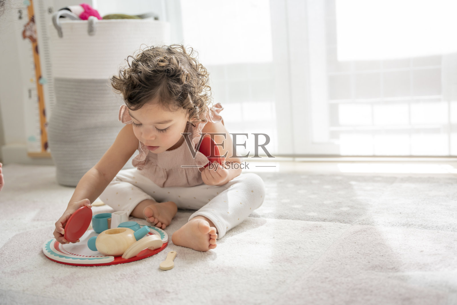 2岁的小女孩坐在房间的地板上玩一个模拟茶和咖啡的木制玩具照片摄影图片