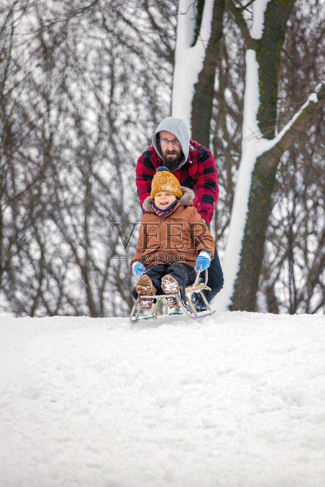 父子俩准备乘雪橇下山。垂直图照片摄影图片