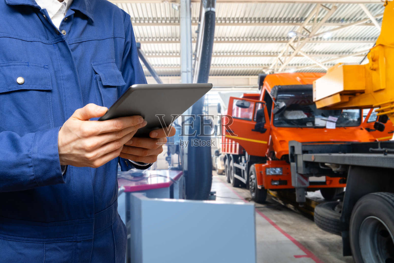 一名军人在车库的卡车背景上拿着数码平板电脑。照片摄影图片