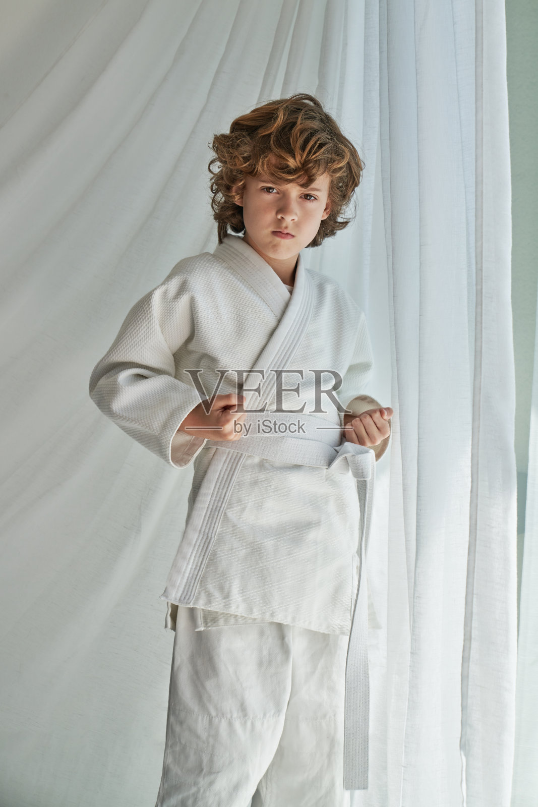 穿着和服的自信的青春期前的孩子在窗边练习空手道照片摄影图片