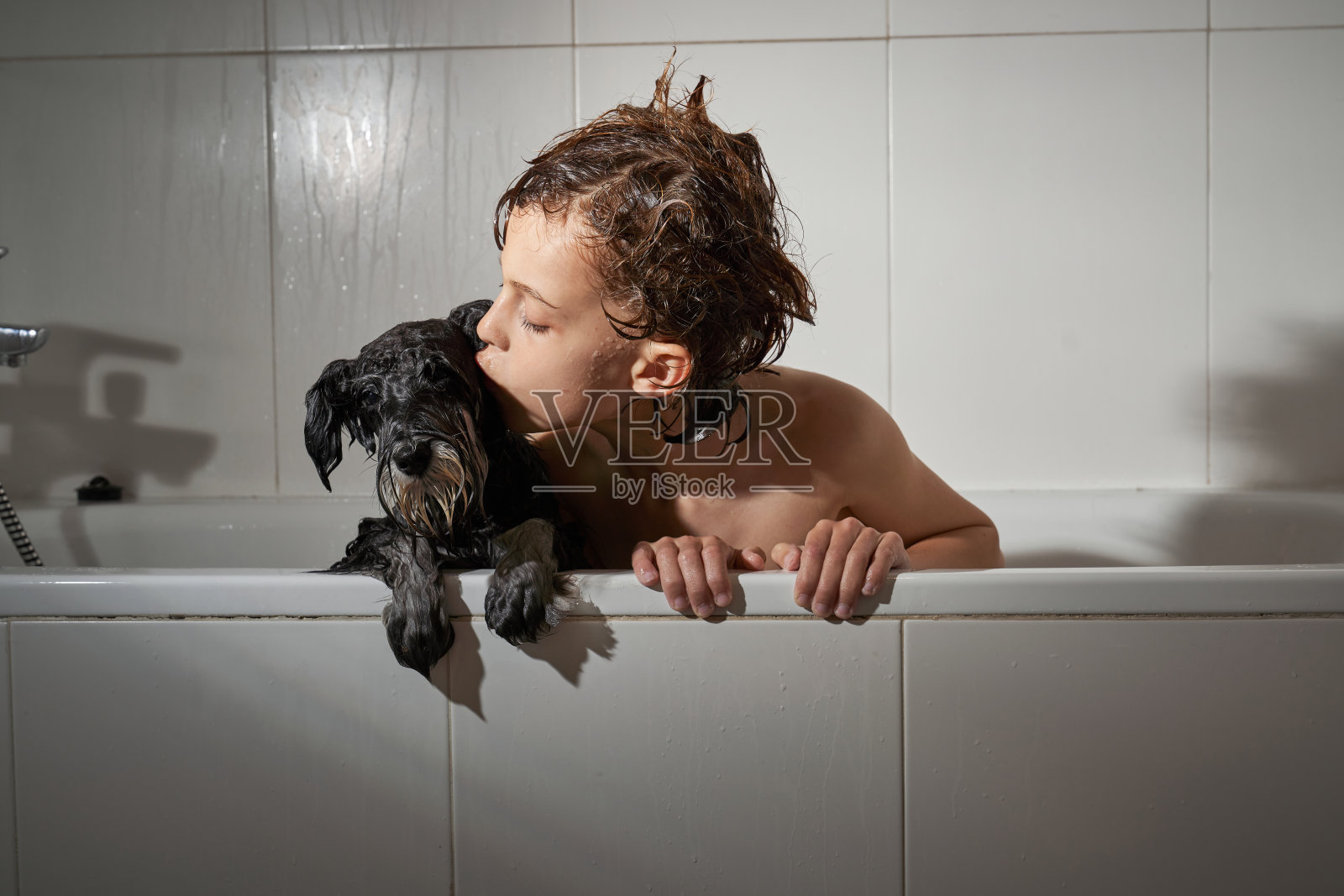 男孩在浴缸里亲吻狗照片摄影图片