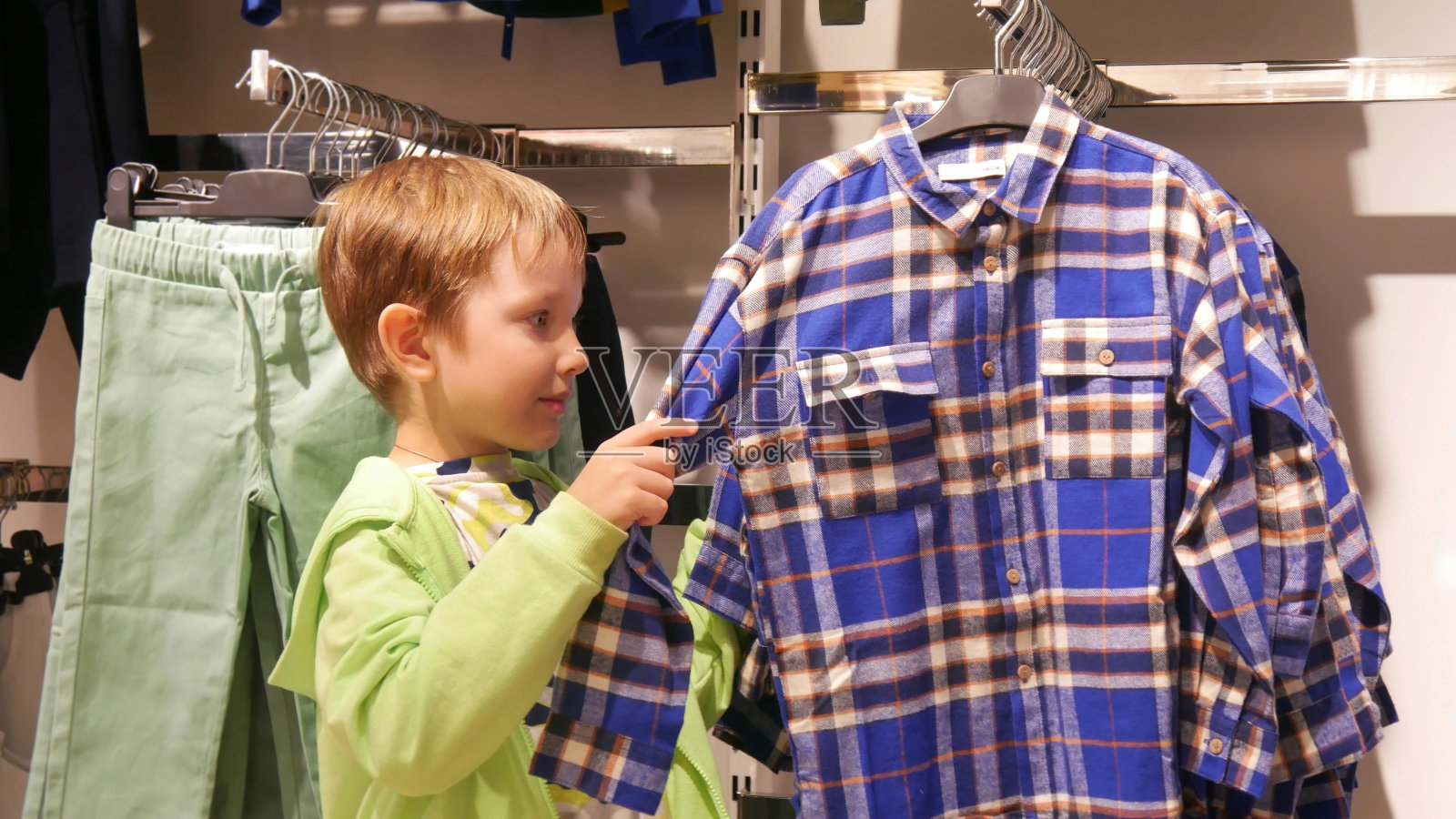 一个可爱的男孩在服装店挑选一件格子衬衫照片摄影图片