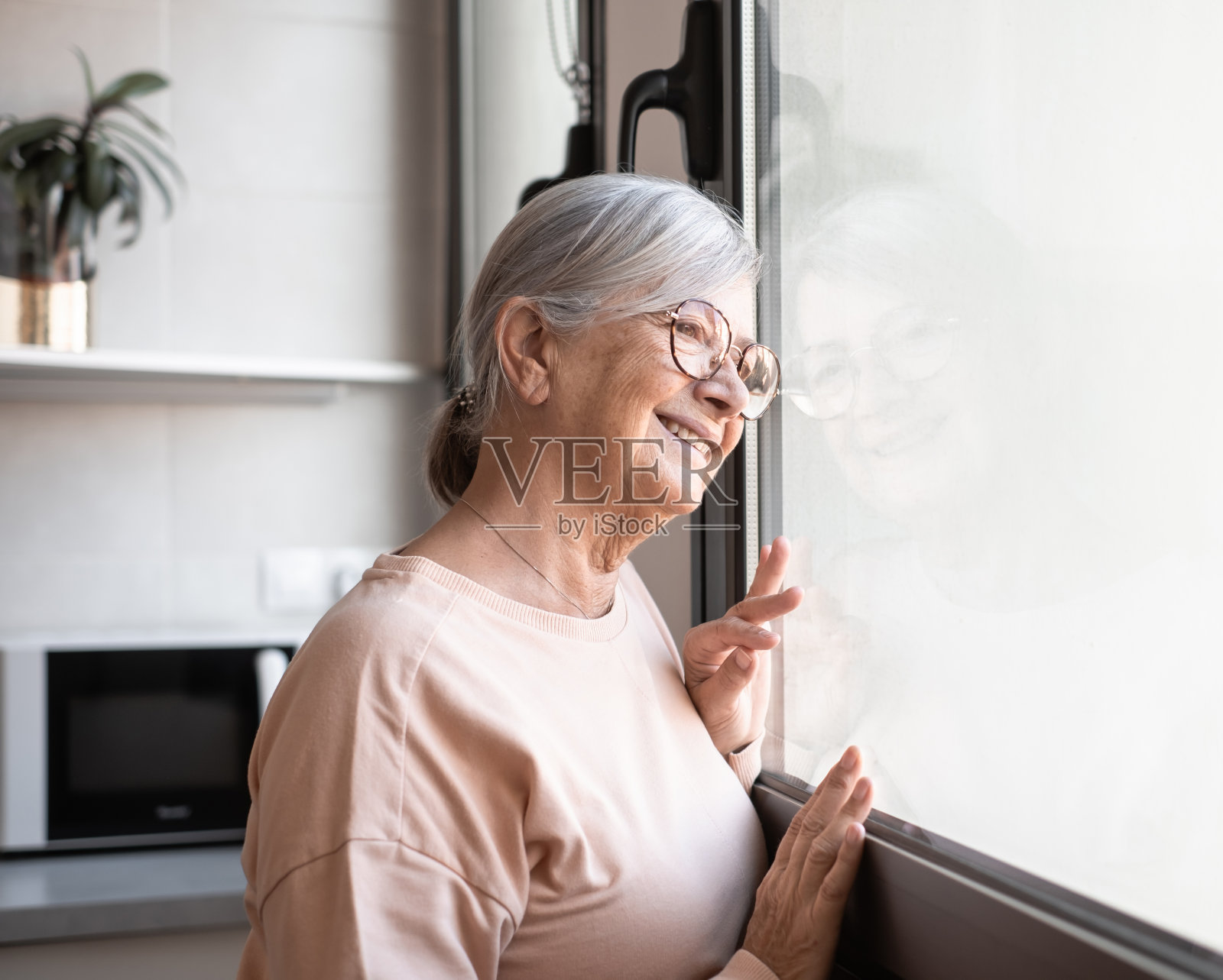 快乐的中老年退休妇女站在窗前,望着远方,回忆着美好的回忆,享受着宁静的时刻照片摄影图片