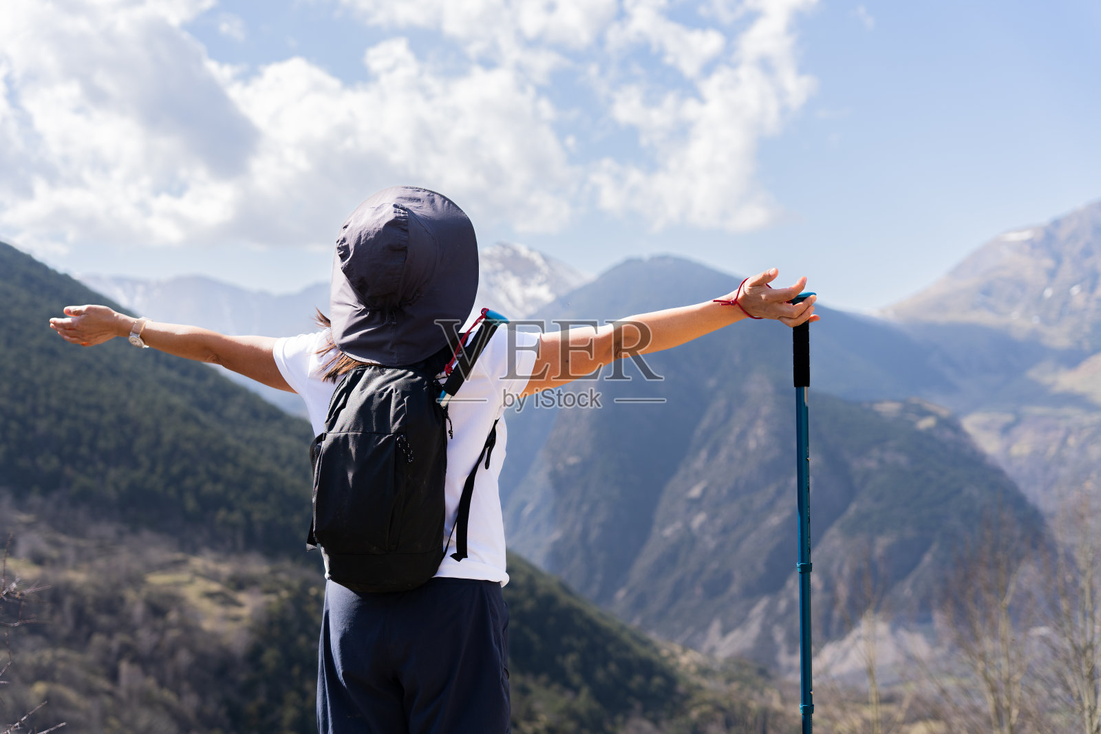 在西班牙加泰罗尼亚比利牛斯山脉徒步旅行的一天里,背着背包和登山杖的陌生女人在美丽的高山景观前张开双臂照片摄影图片