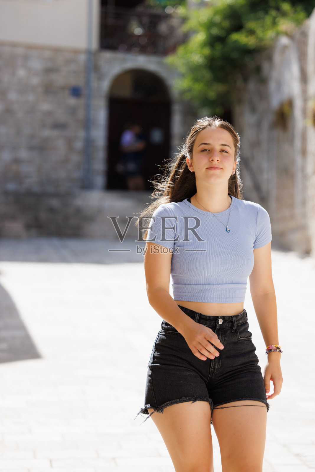 美丽的少女在阳光明媚的日子里,走在古老岛屿小镇的石头铺成的小巷里照片摄影图片