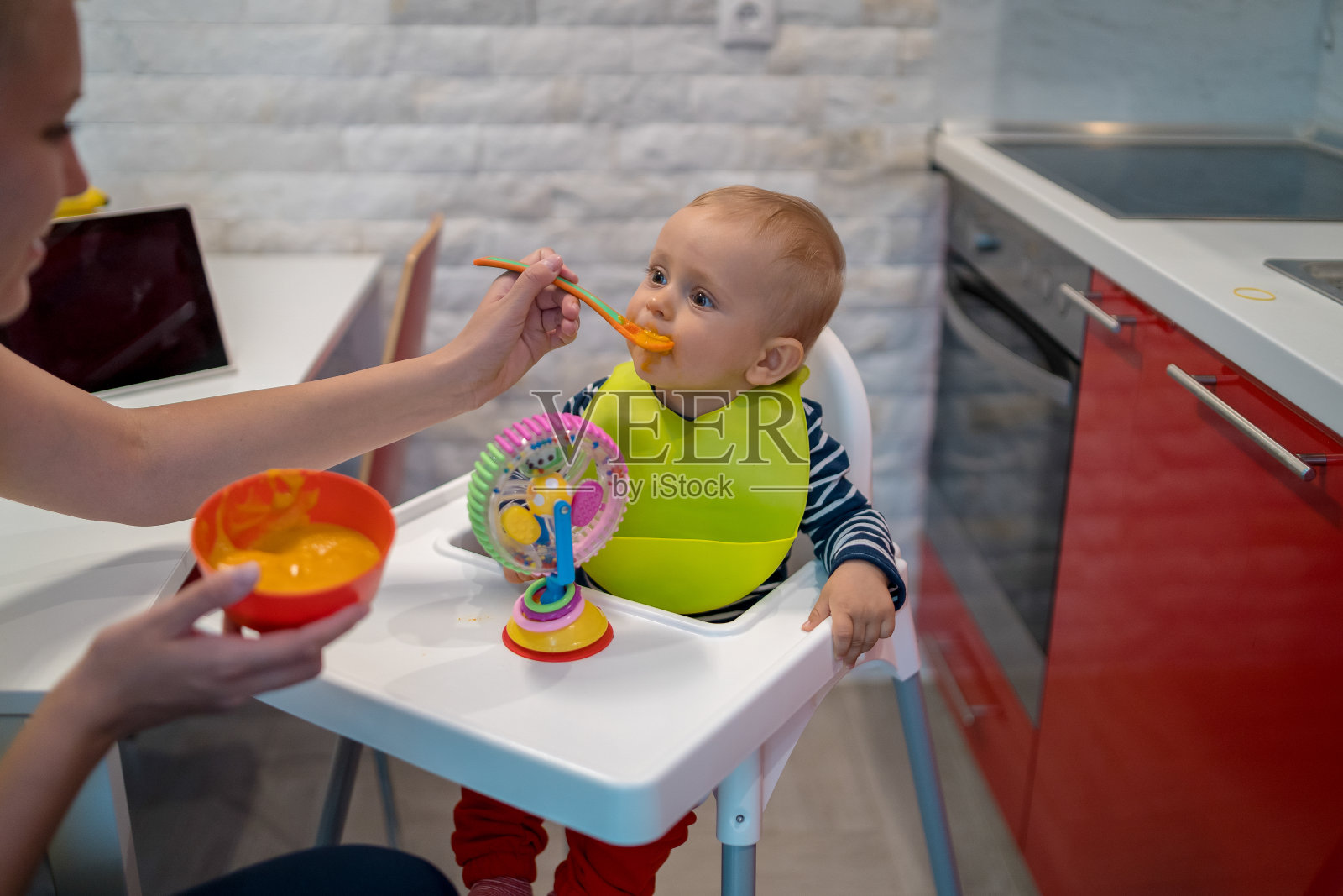 母亲在厨房用勺子喂她的小男孩照片摄影图片