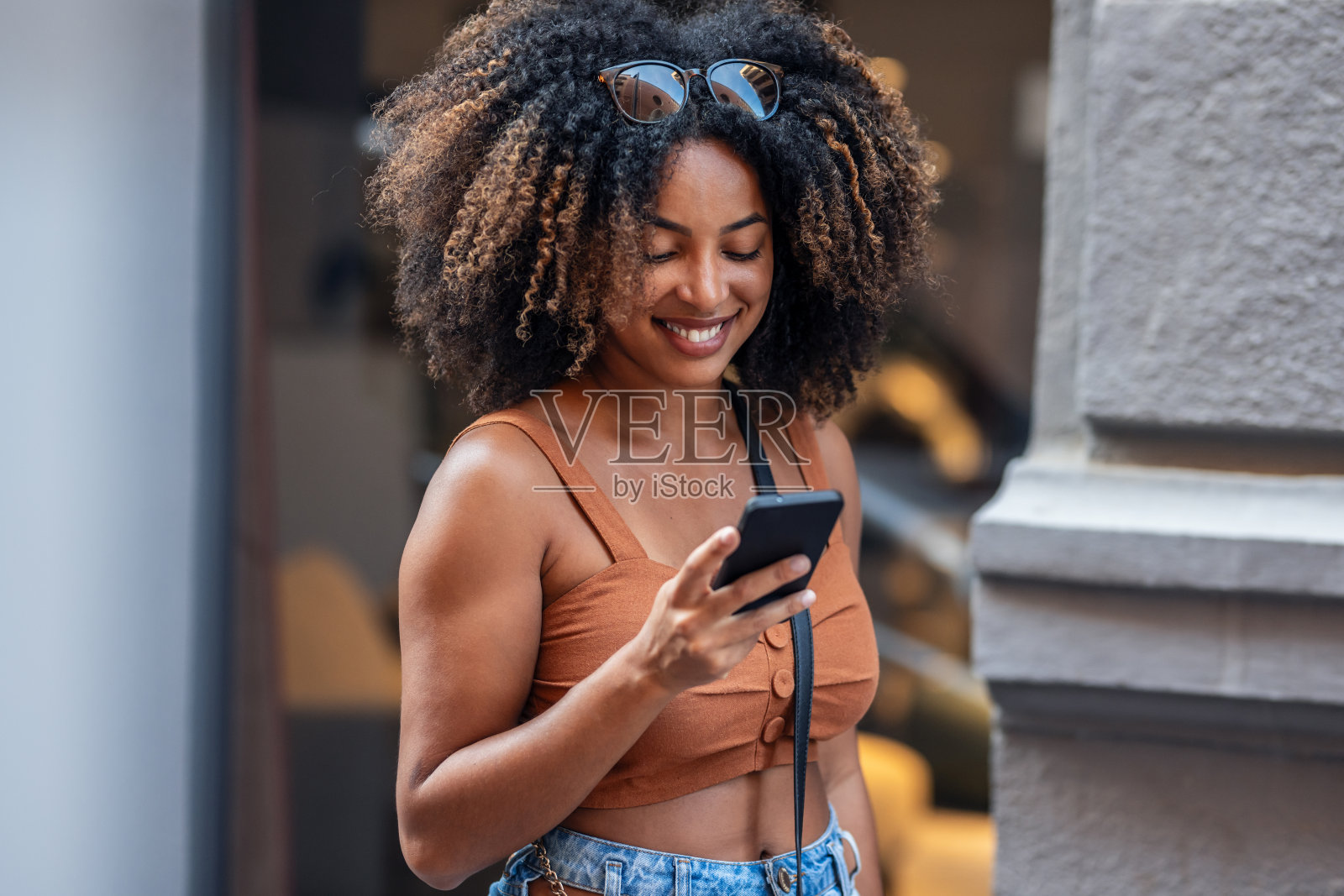 微笑的女人一边拿着购物袋一边用智能手机走在城市里照片摄影图片