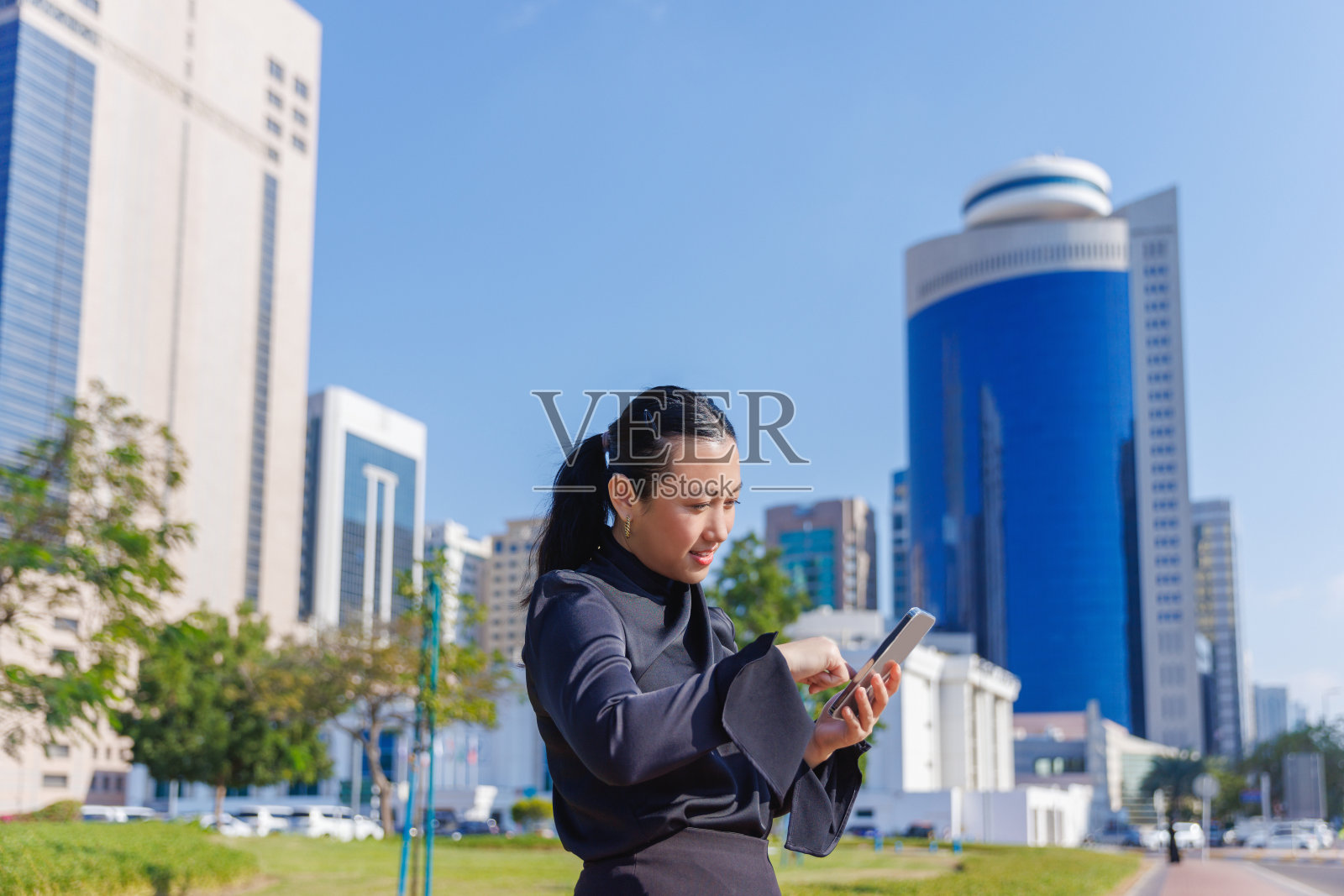 阳光明媚的日子里,在公园用手机的亚洲女性照片摄影图片