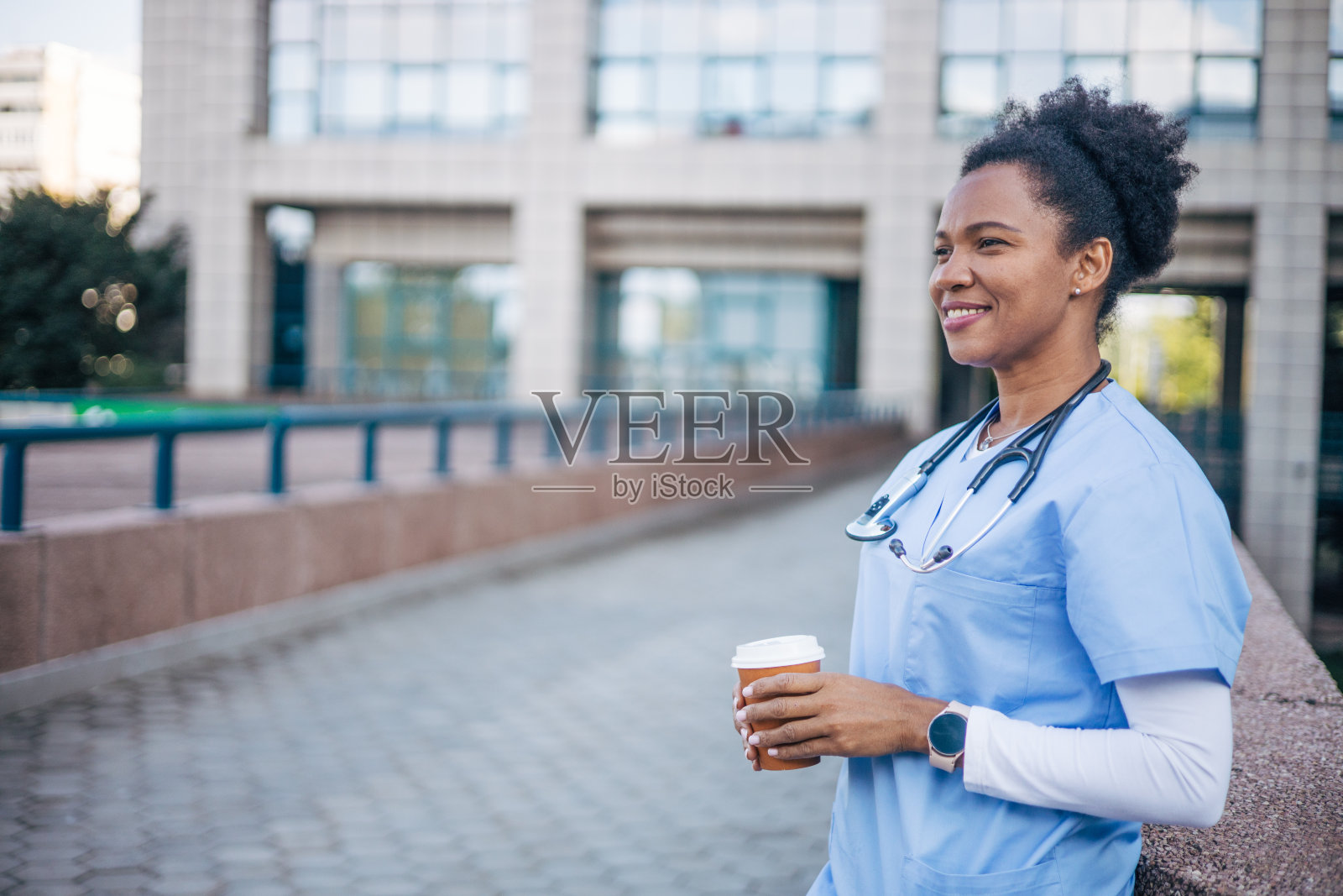 女医生站在外面,拿着咖啡杯。照片摄影图片