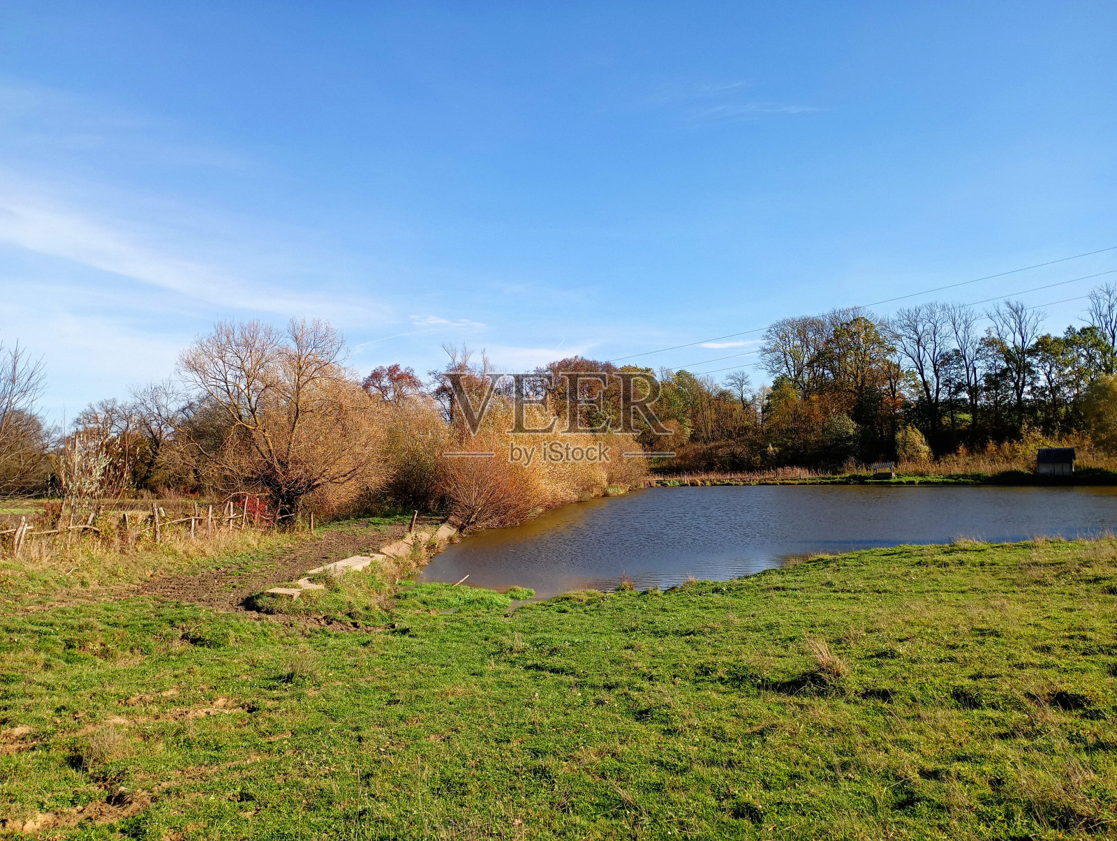 从长满绿草的平原上,可以看到一个心形的池塘,池塘的一边长着树木,另一边则陡峭地矗立在山上。日落时的水库照片摄影图片