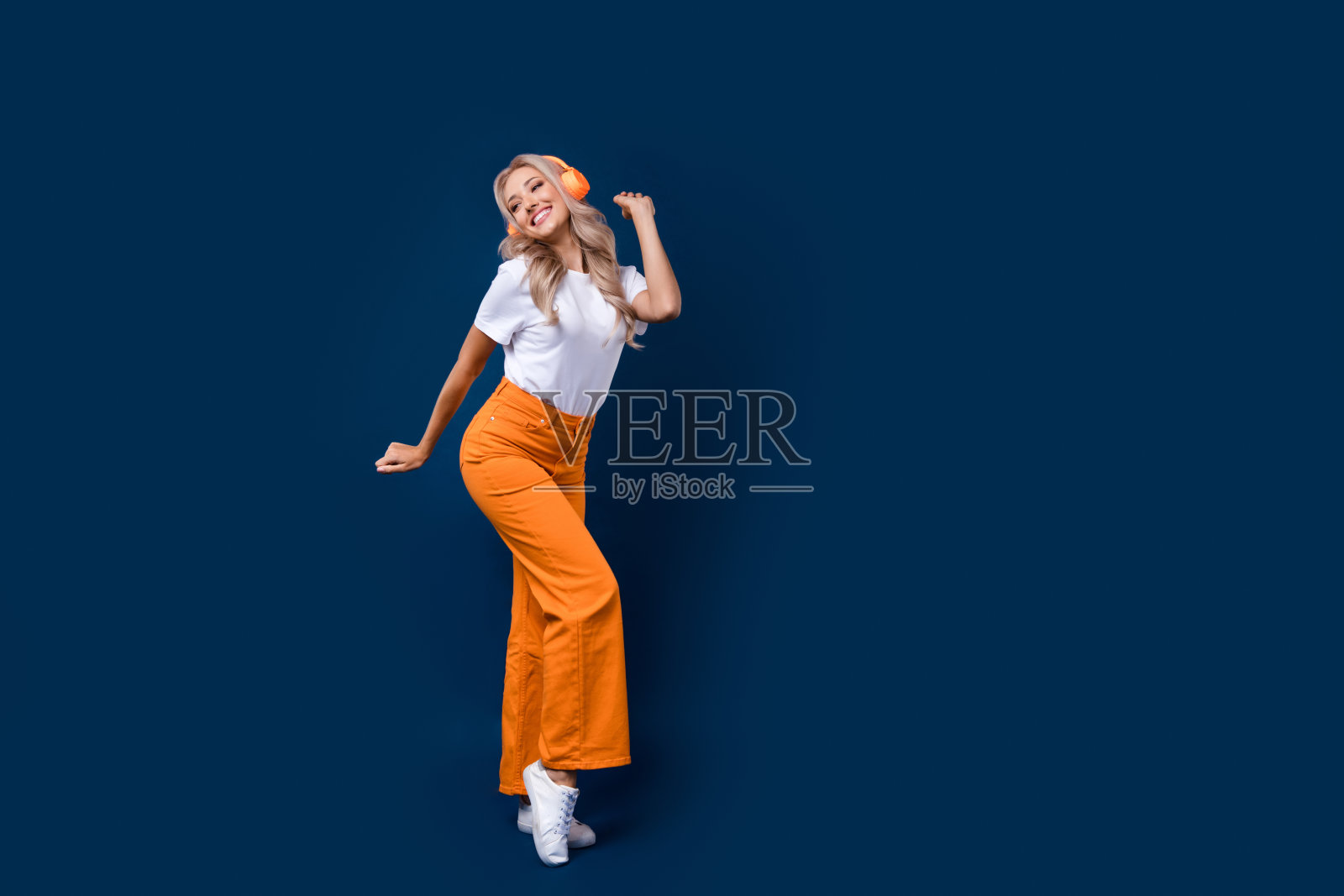 开朗可爱的女孩听mp3播放器无线耳机的全长照片,在深蓝色的背景空空间隔离照片摄影图片