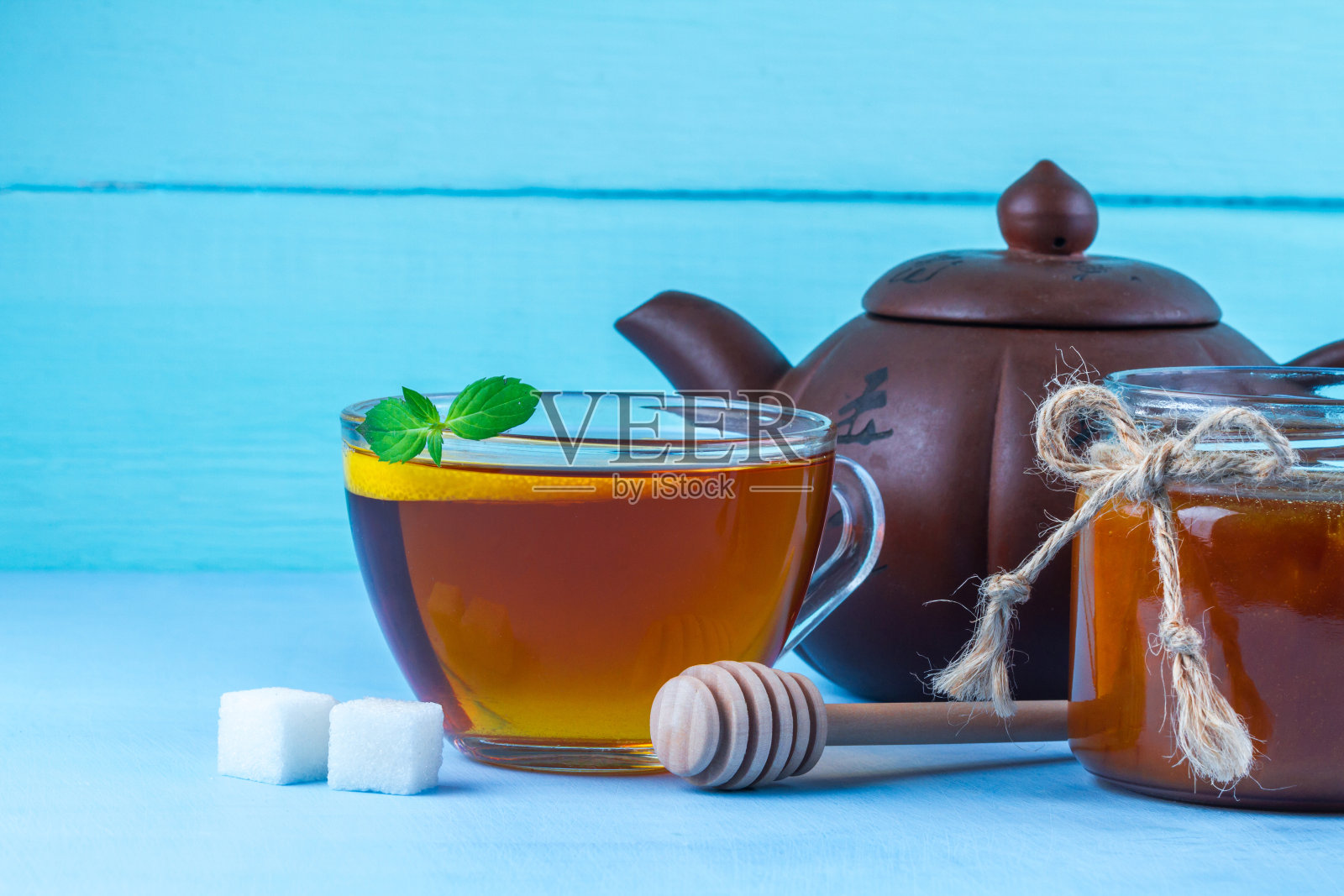 茶喝。一杯热茶,加一片新鲜的薄荷和多汁的柠檬,一个茶壶,自制的蜂蜜罐和蜂蜜勺,蓝色背景照片摄影图片