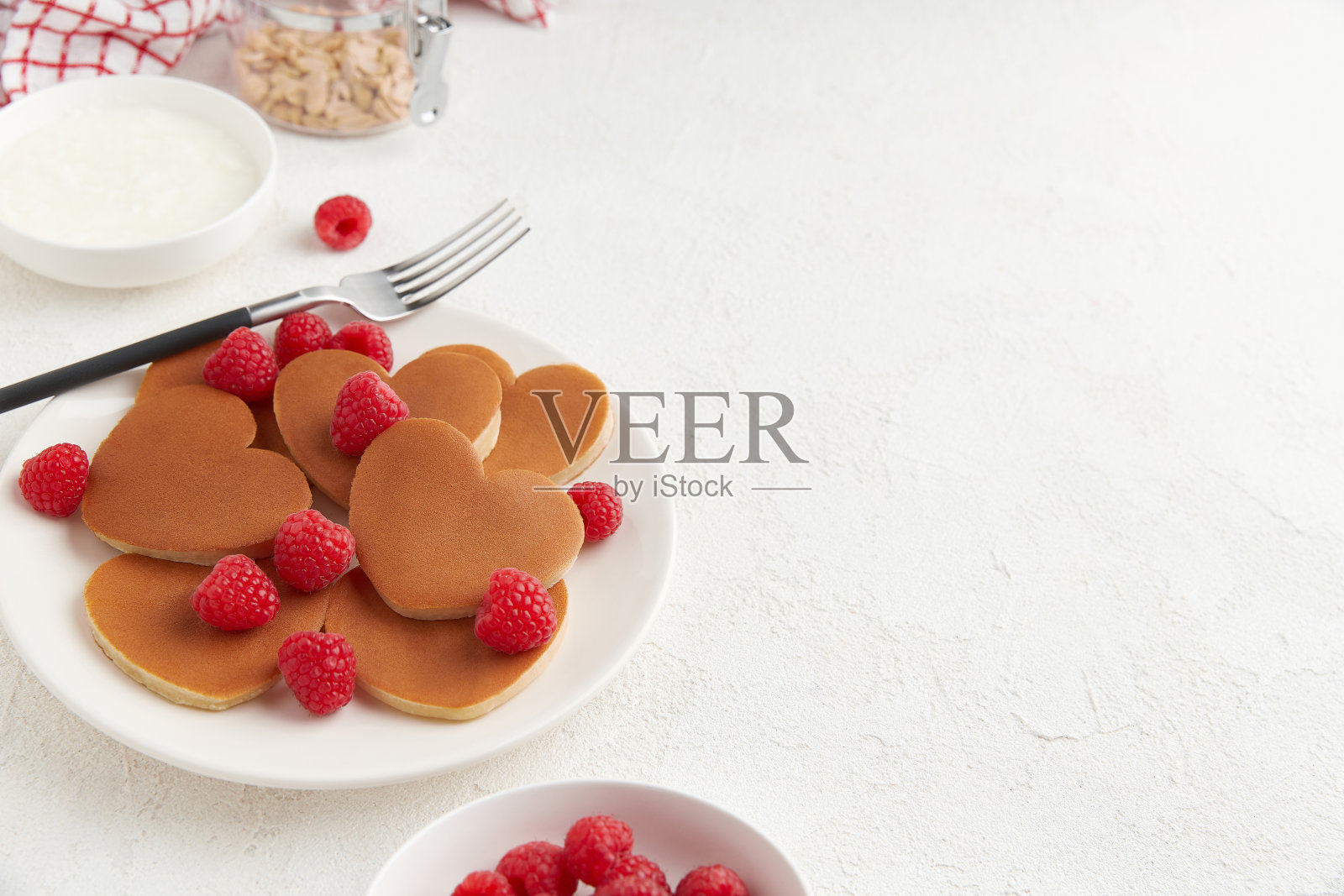 一堆带覆盆子的心形煎饼和一把叉子放在白色的盘子上,白色的背景照片摄影图片