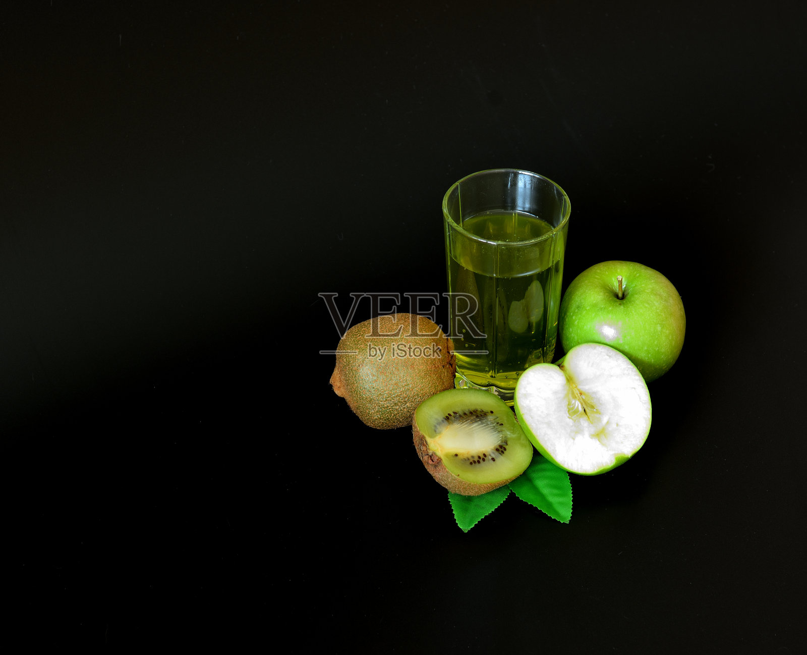 一杯黑色背景的鲜榨果汁,旁边是几片成熟的猕猴桃和一个成熟的青苹果。照片摄影图片