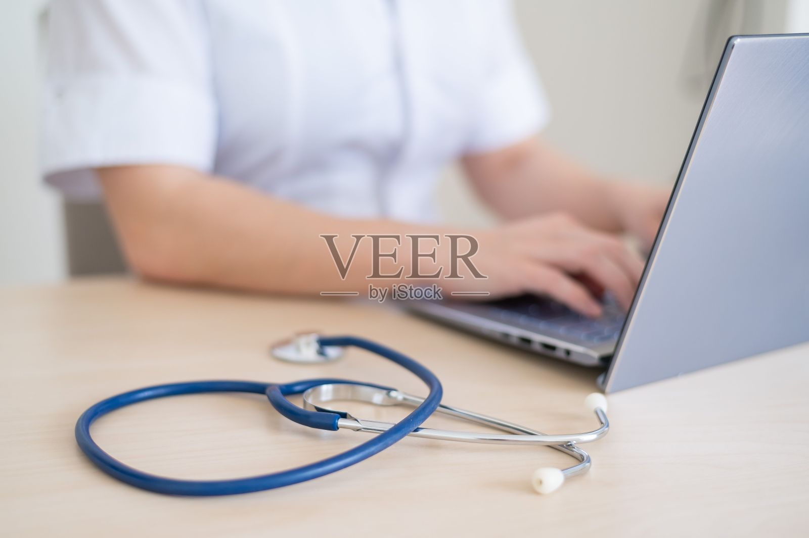 穿制服的女医生用的是笔记本电脑。不知名的医务人员在桌子上的电脑上写报告。裁剪。照片摄影图片