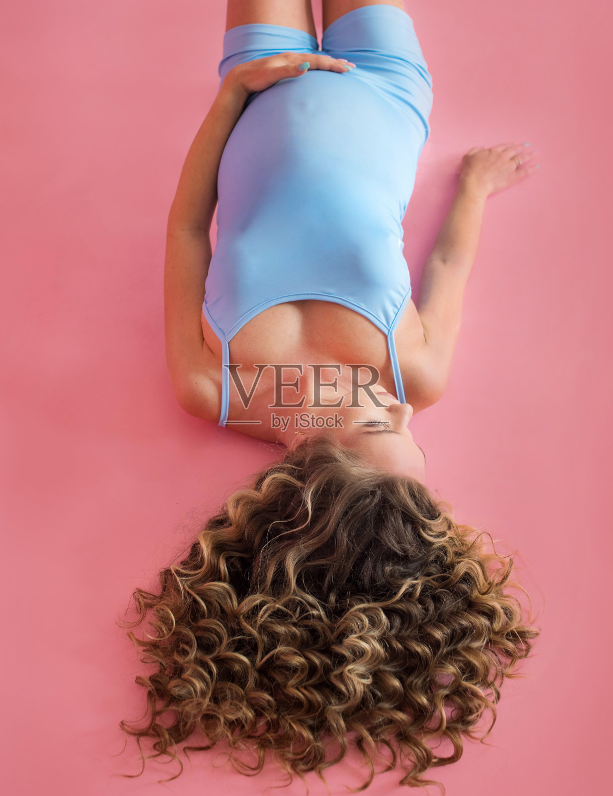 趴在粉色背景上怀孕的女孩,俯视图,前景是卷发照片摄影图片