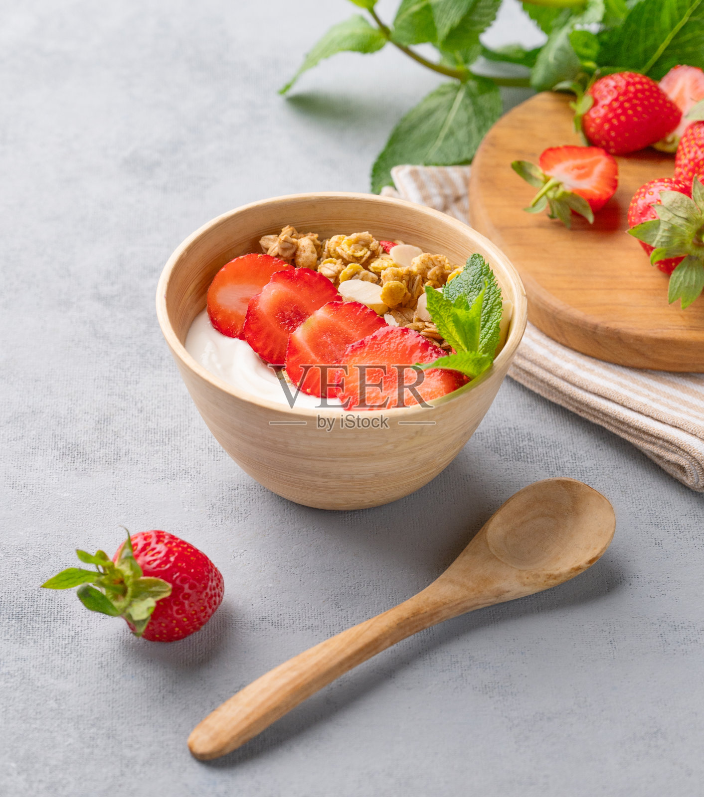 天然酸奶与什锦麦片和草莓在蓝色背景的碗与新鲜浆果和薄荷。照片摄影图片