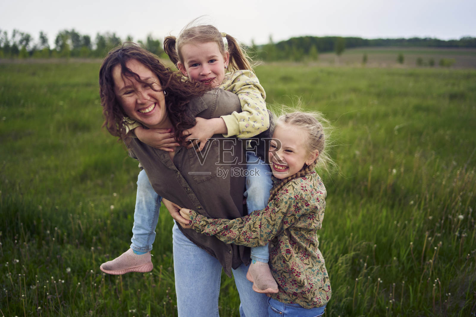 一位母亲把女儿们抱在背上,玩着骑马的游戏,亲吻和拥抱照片摄影图片