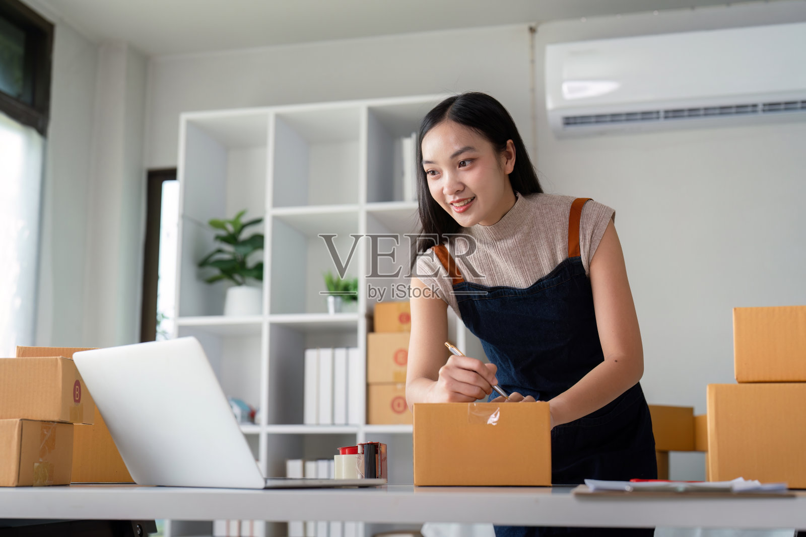 一位亚洲妇女在网上商店查看顾客地址和盒子上的包裹信息。网上购物概念照片摄影图片