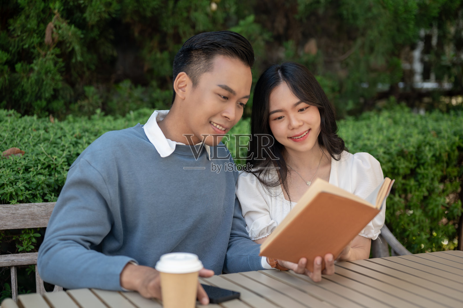 可爱的亚洲小情侣在公园里依偎而坐。照片摄影图片