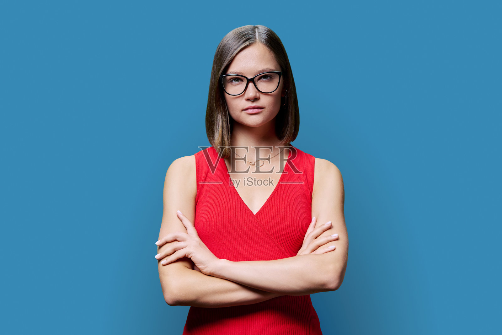 年轻的严肃自信的女人在蓝色工作室背景的红色照片摄影图片