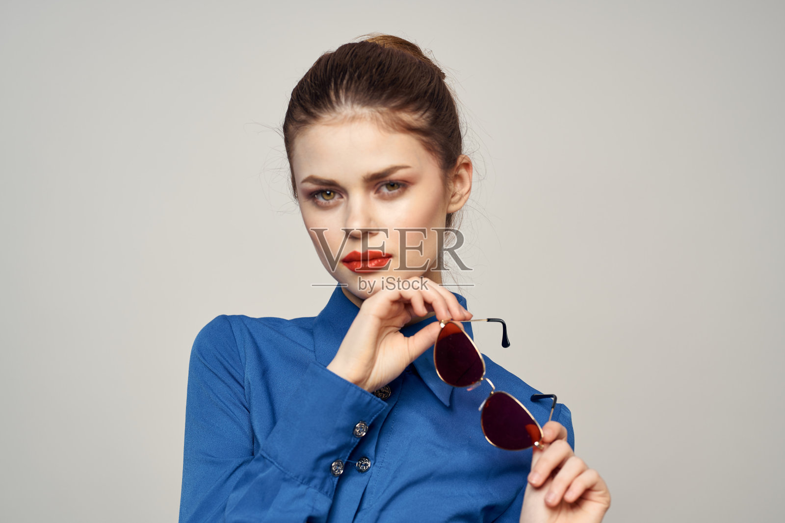 戴着太阳镜,穿着蓝色衬衫的时尚女子在浅色背景裁剪的视图上用手比划着照片摄影图片