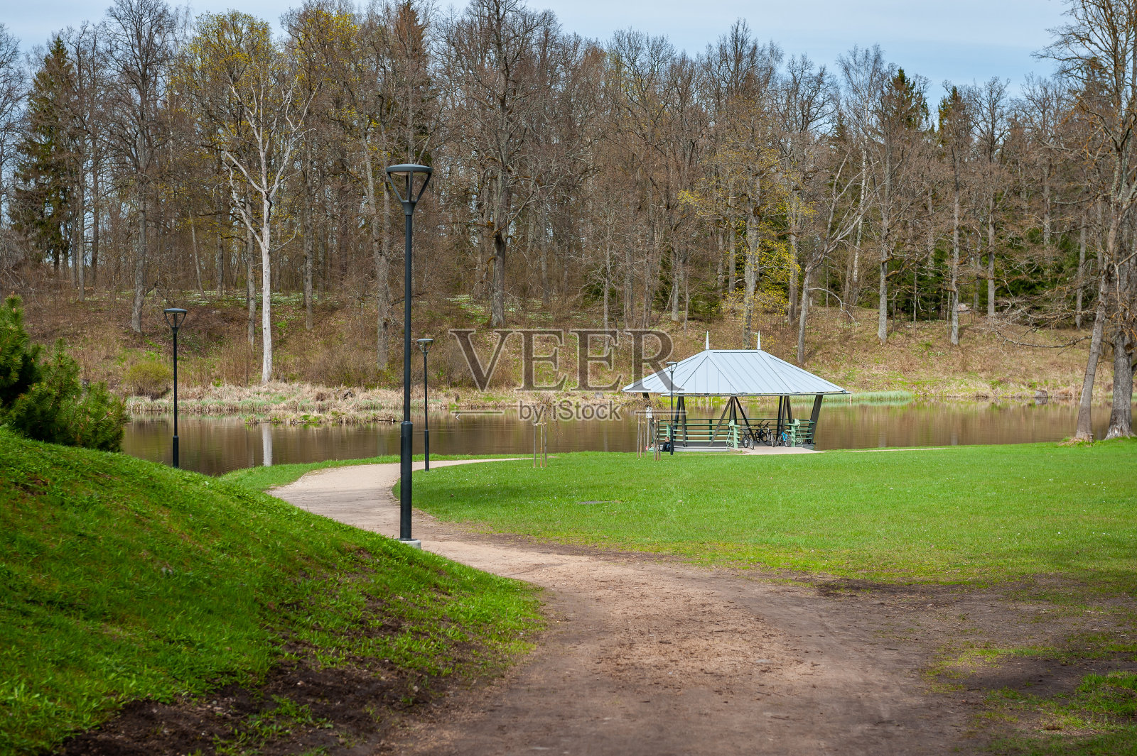 一个绿色的凉亭,有一个屋顶,在公园里,在一个安静的湖边。照片摄影图片