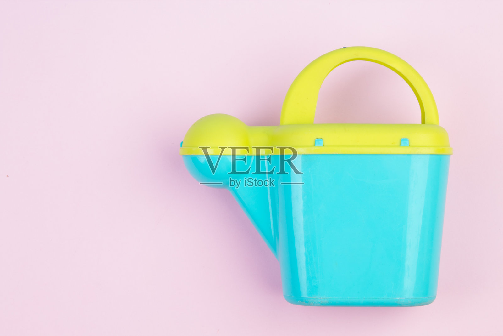 孩子们在沙盒或花园里玩耍时用的塑料喷壶。用于浇花的彩色喷壶,在粉红色背景上突出显示,特写。照片摄影图片