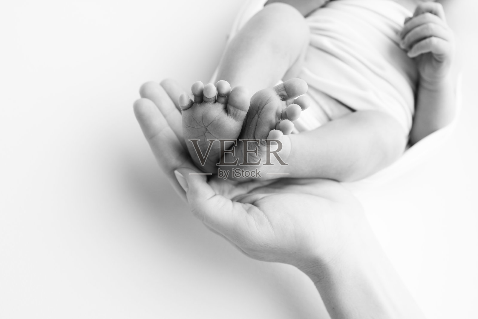 爸爸的手掌,妈妈都抱着刚出生的婴儿的脚。新生儿的脚放在父母的手掌上。工作室微距黑白照片的一个孩子的脚趾,脚跟和脚。照片摄影图片