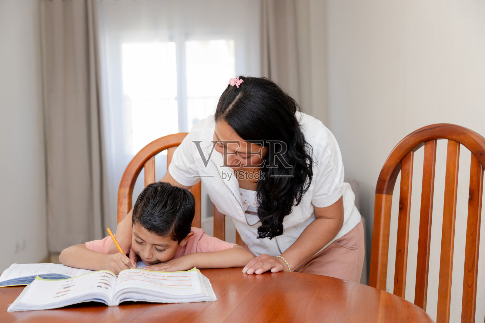 妈妈帮助她的小儿子做作业——妈妈和她的儿子一起学习——老师和她的学生教他写字——在家上学照片摄影图片