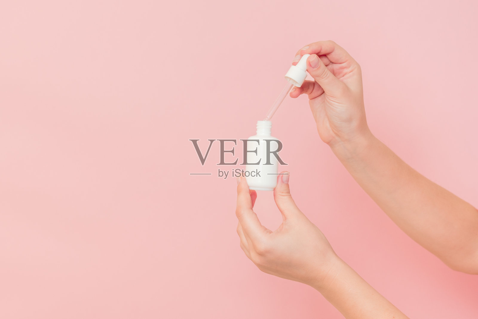 手持玻璃化妆品瓶血清(透明质酸和胶原蛋白)在粉红色的背景。美丽的概念照片摄影图片