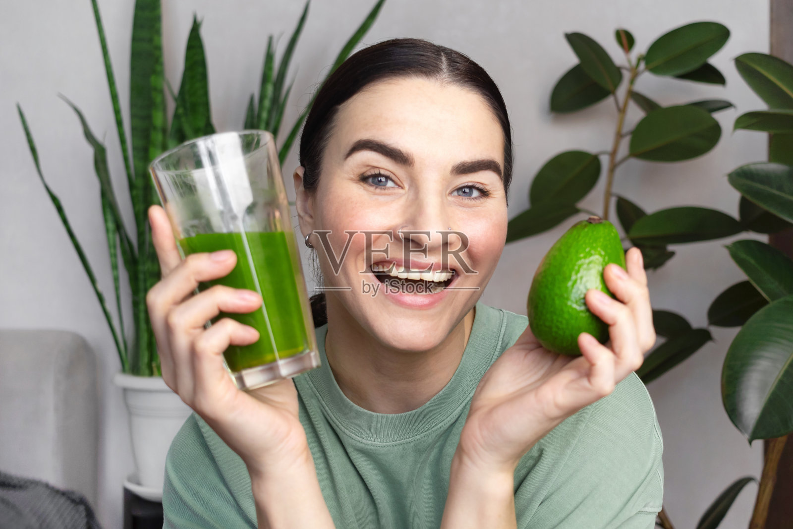 女人很高兴,她微笑着给我看绿麦草饮料和牛油果。健康生活理念,绿色健康蔬果。照片摄影图片