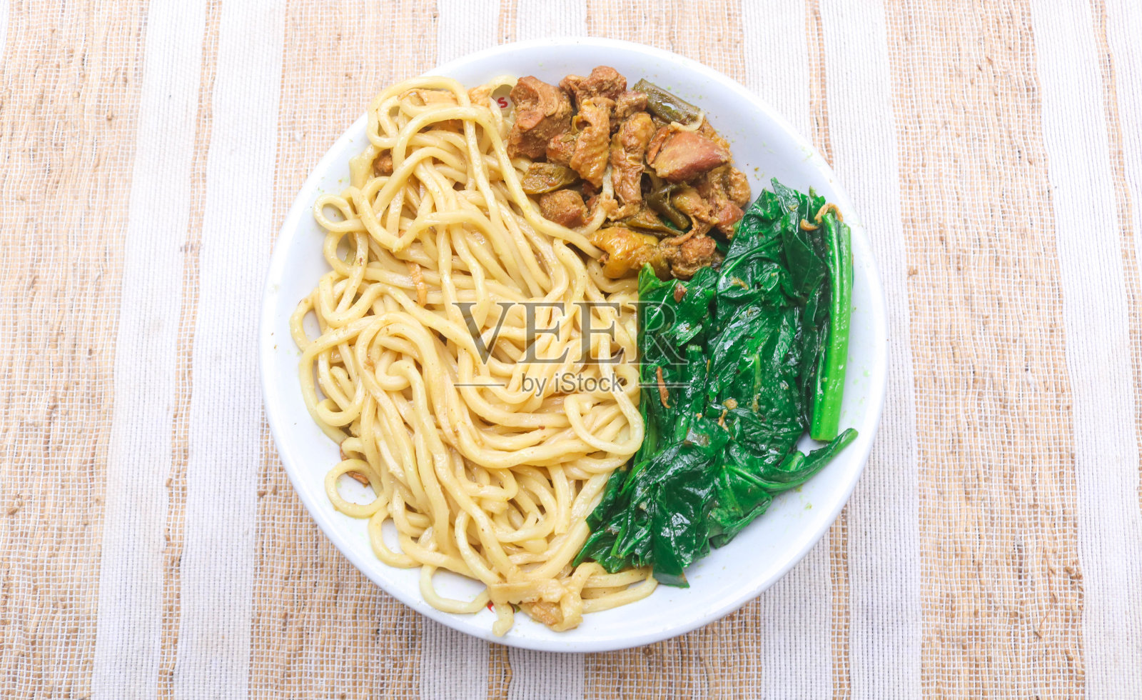 印尼的鸡肉面是一种用鸡肉末、煮熟的芥菜和酱油放在木桌上的白色碗里的面条照片摄影图片