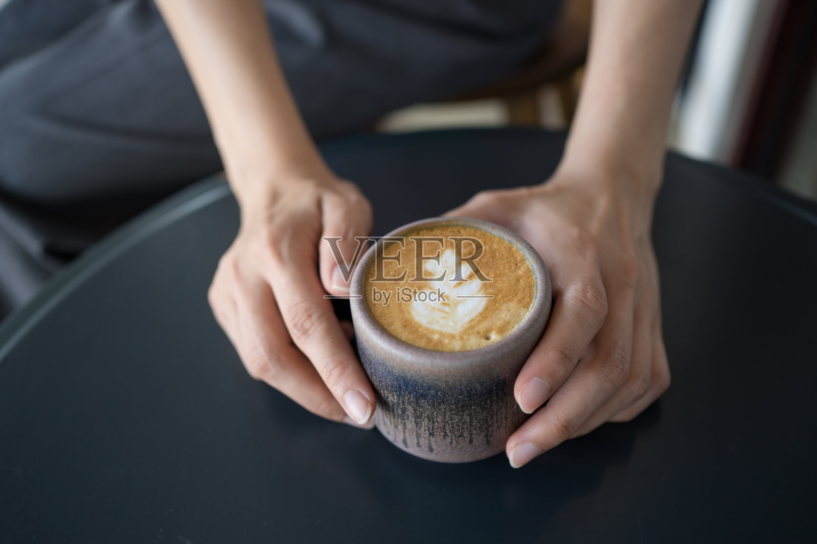 女人的手拿着一杯拿铁咖啡,在黑色的桌子上有拿铁艺术。照片摄影图片