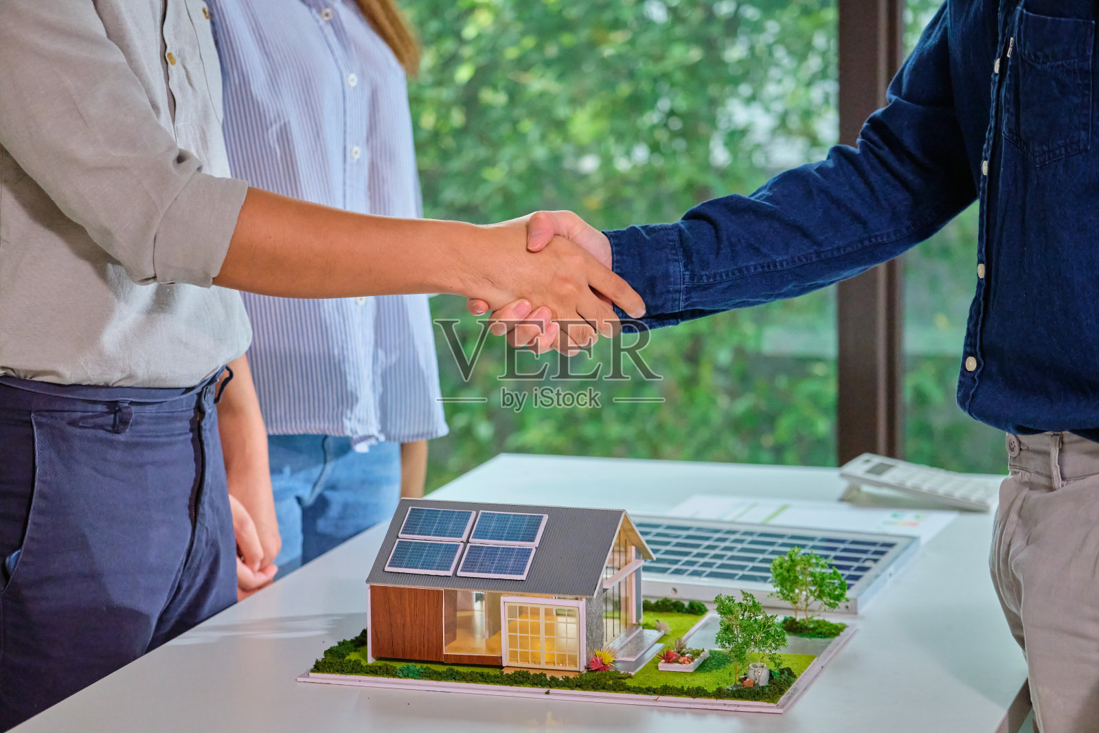 近距离握手的夫妇与太阳能销售工程师在一个家庭模型上的太阳能电池板成功的交易协议象征着绿色能源的可持续发展照片摄影图片