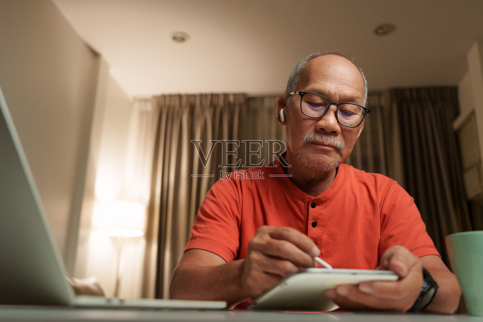 资深亚洲商人专注于工作,在家办公室使用笔记本电脑和做笔记照片摄影图片