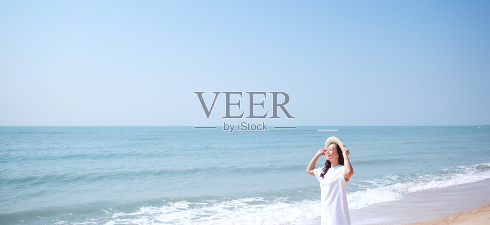 一名年轻女子在沙滩上散步的肖像,背景是大海和蓝天照片摄影图片